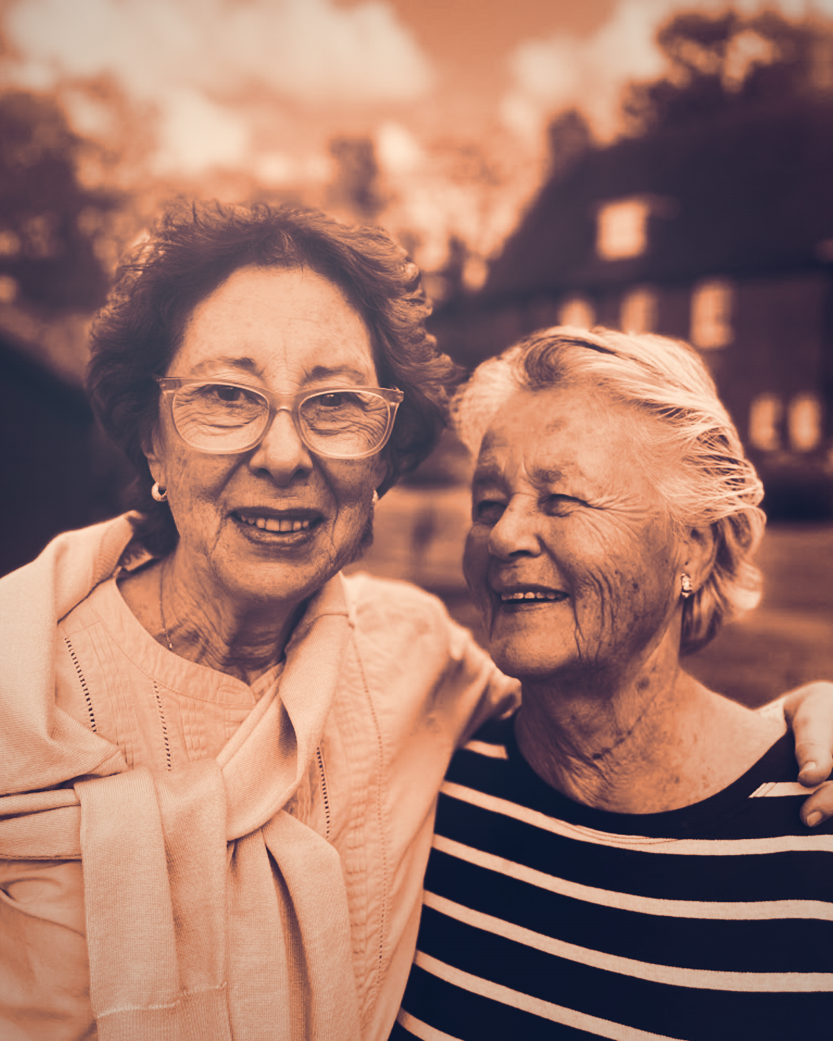 Two older women standing together outdoors, arms around each other
